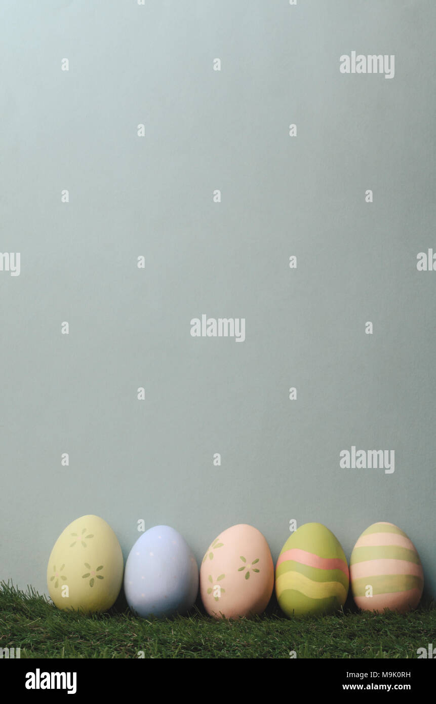 A row of decorated eggs in different colours on artificial grass against blue grey background for Easter. Filtered to give muted, retro style. Stock Photo