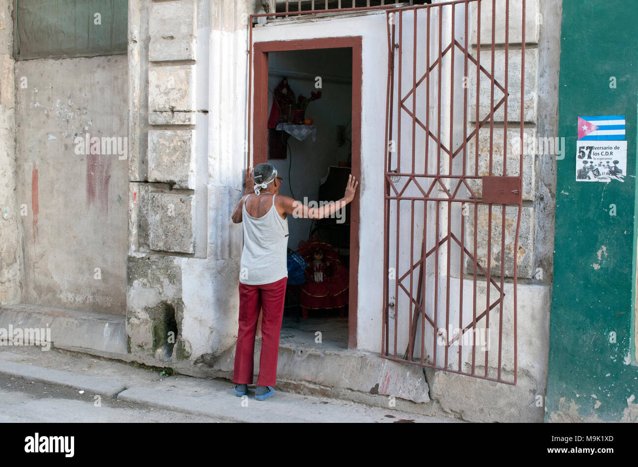 A woman stands on the sidewalk looking into the open doorway of a building in Old Havana, Cuba. Stock Photo