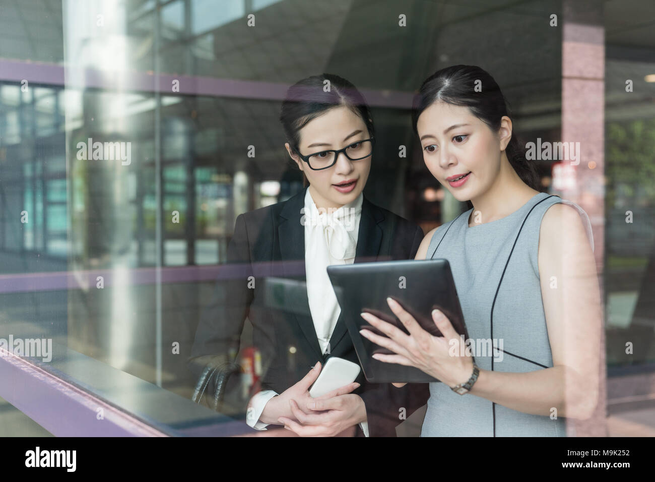Asian supervisor showing their product to client standing aside the glass door. Using the tablet inside the modern and advanced company. Stock Photo