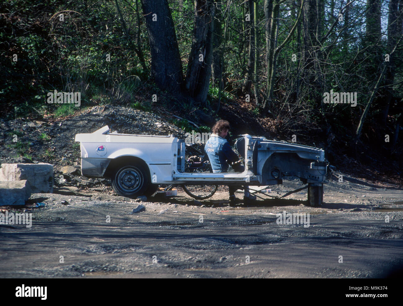 Man sitting on a car that has been stripped and left abandoned at a park in Seattle Stock Photo