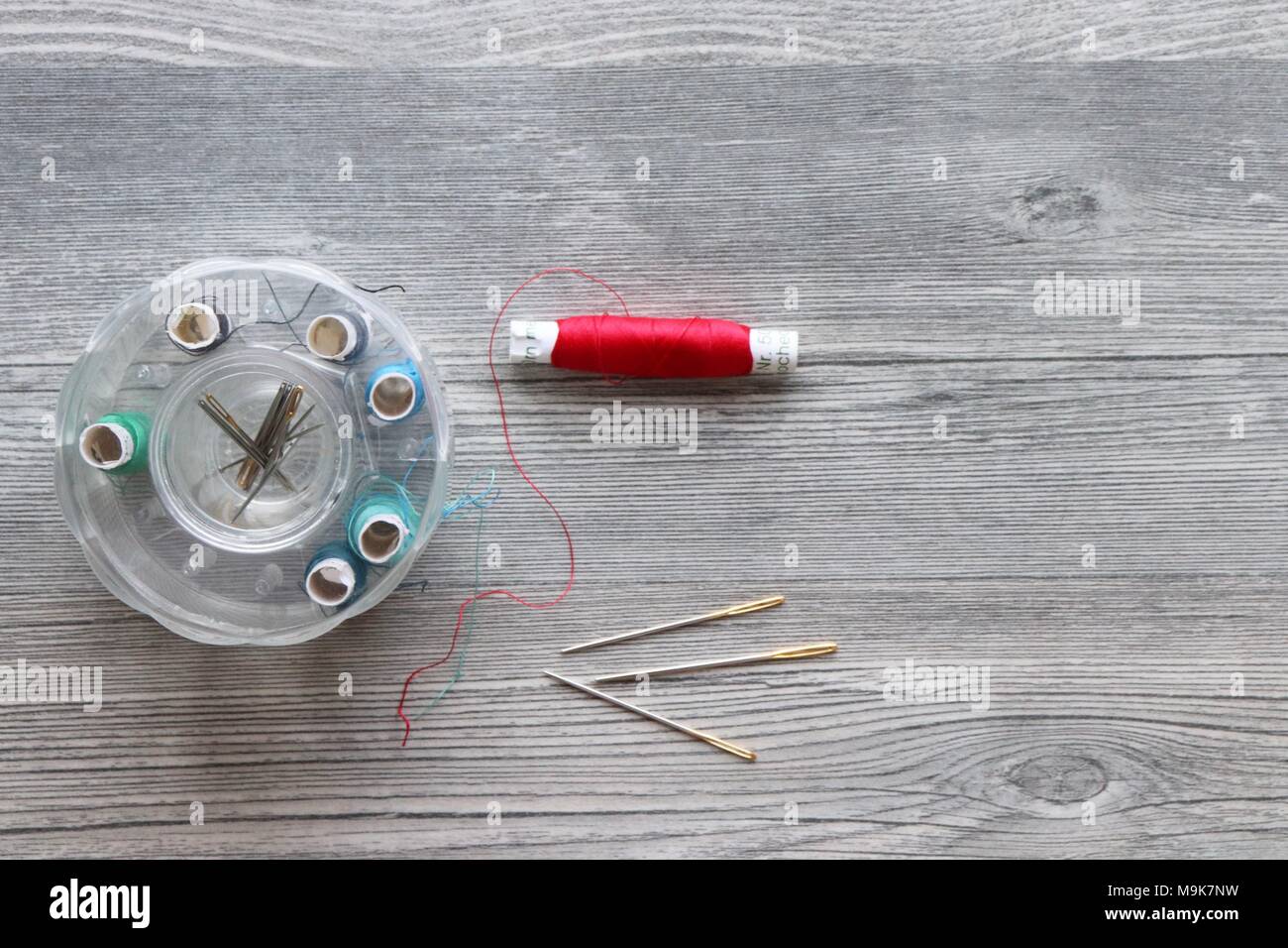 Red thread, needles, sewing kit on grey plank background with space for