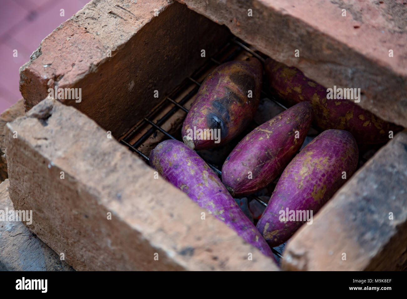 Grilled raw sweet potatoes on charcoal grill inside DIY brick oven