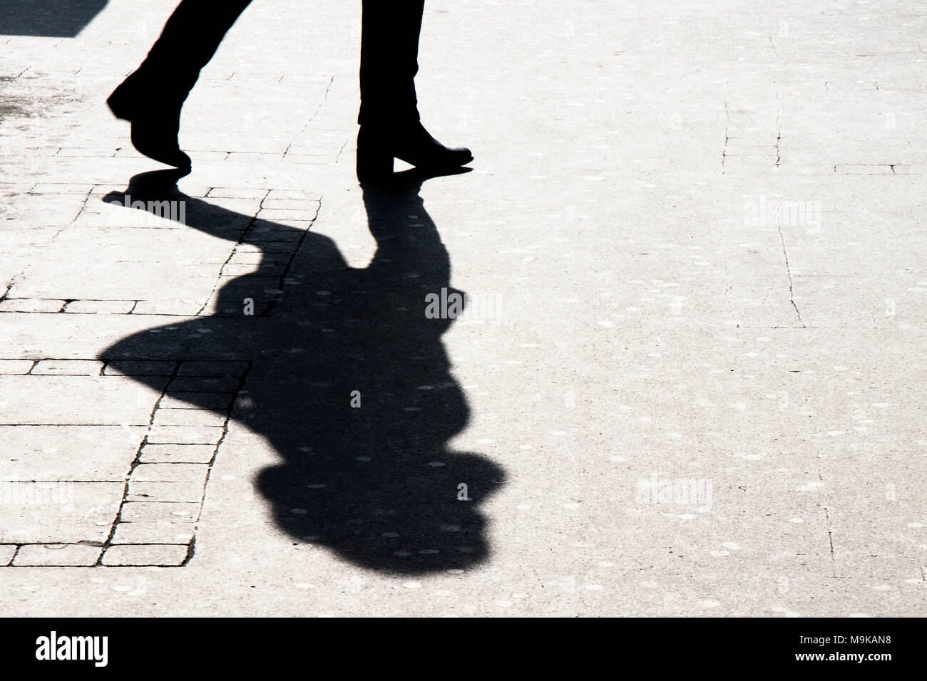 Silhouette shadow of woman legs walking city street in black and white Stock Photo