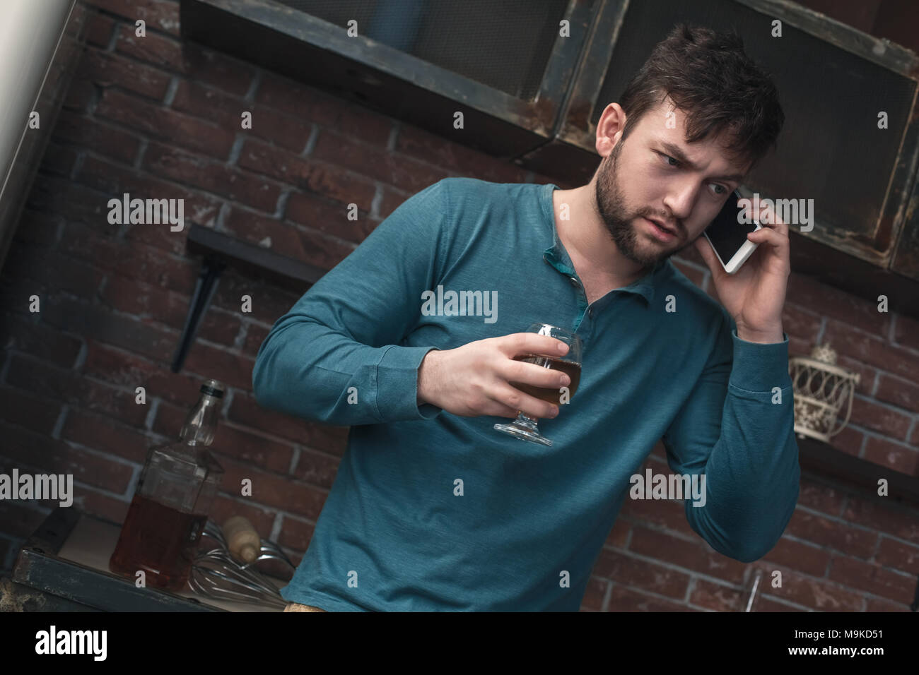 Young man alcohol addiction problems standing using smartphone talking serious conversation drinking whiskey Stock Photo