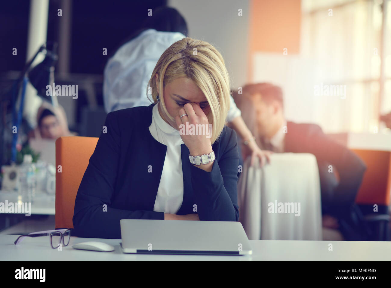 Feeling tired and stressed. Frustrated adult woman keeping eyes closed from fatigue while sitting in office. Stock Photo