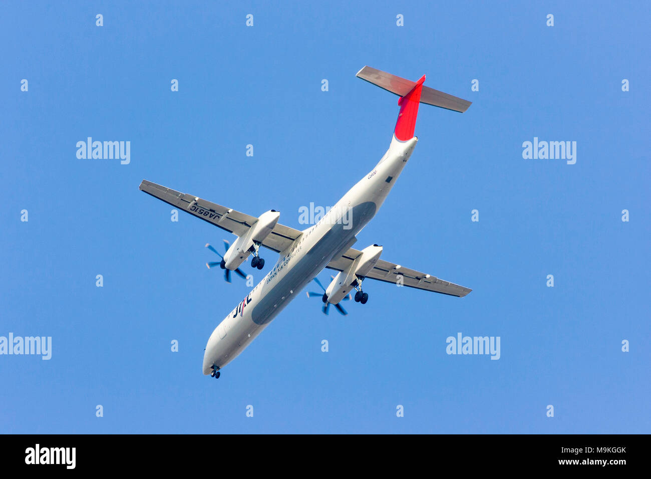 Japanese airline, JAL, Bombardier DHC8-Q100(DH1) in flight, rear view overhead against clear blue sky. Stock Photo