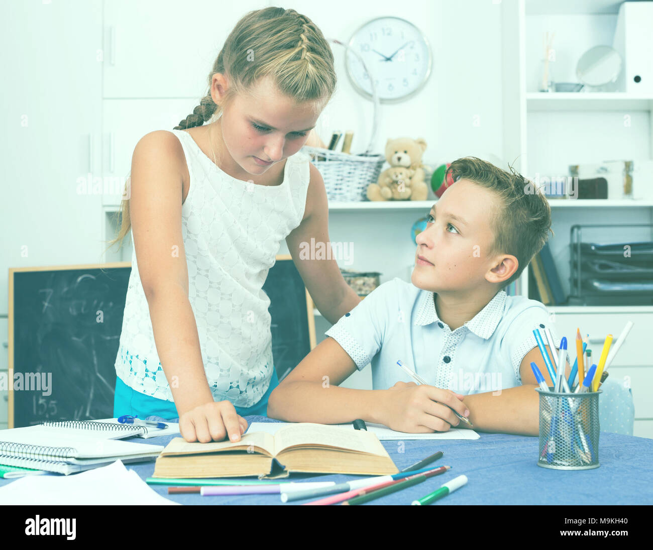 Girl is explaining to boy how to solve homework at home. Stock Photo