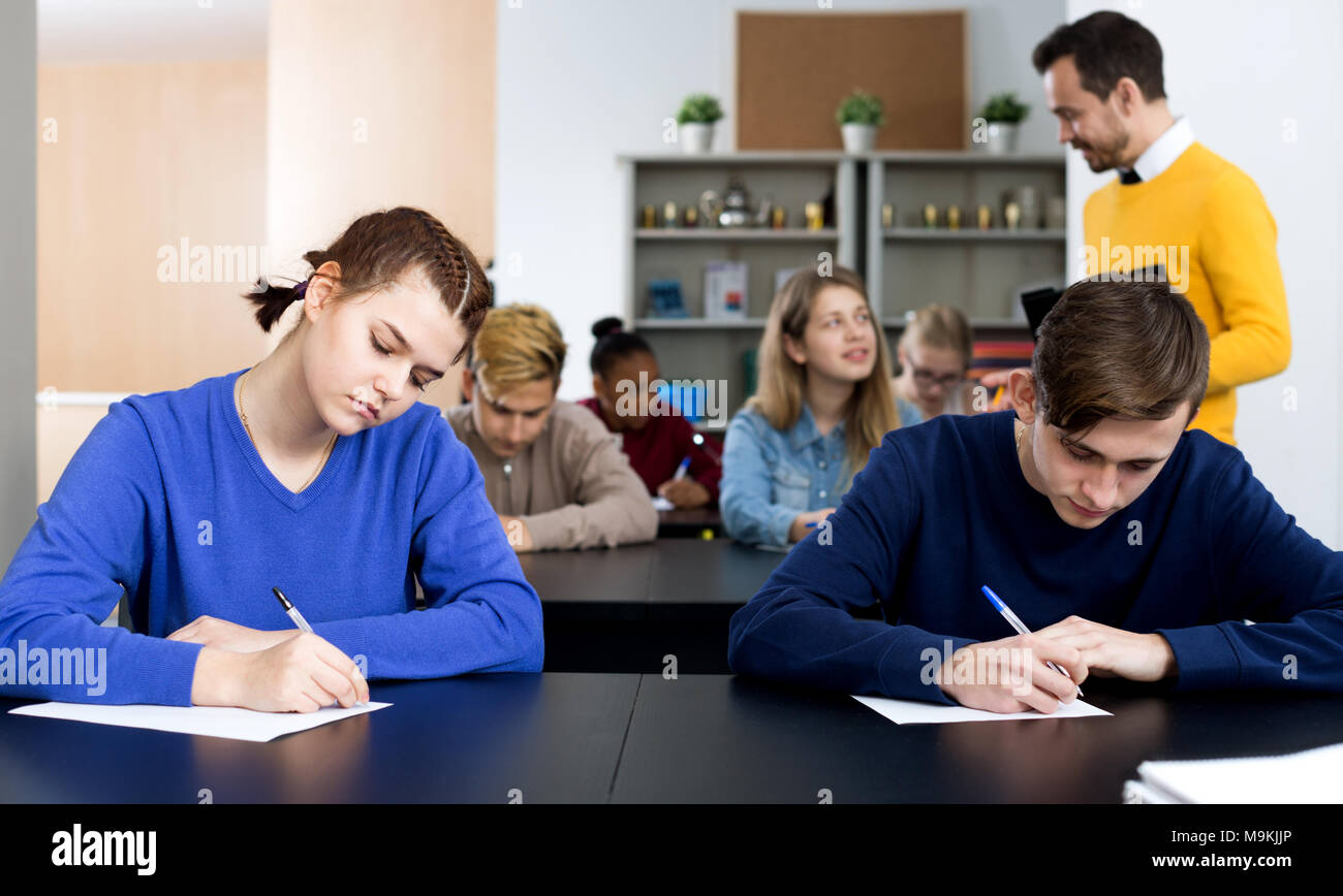 Happy male teacher inspecting working process of students during exam in class Stock Photo