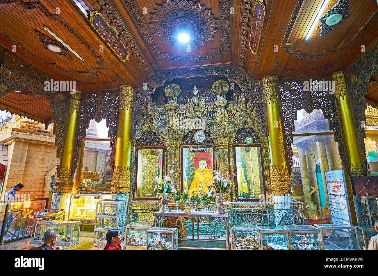 YANGON, MYANMAR - FEBRUARY 14, 2018: The complex decoration of interior of image house - the carved wooden patterns and huge golden columns around the Stock Photo