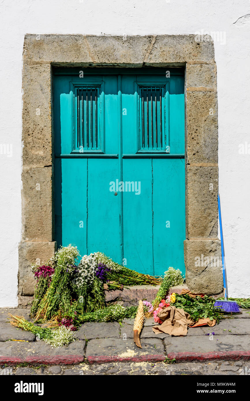 Broom & bundles of flowers strewn on doorstep in front of turquoise door in Guatemala, Central America Stock Photo