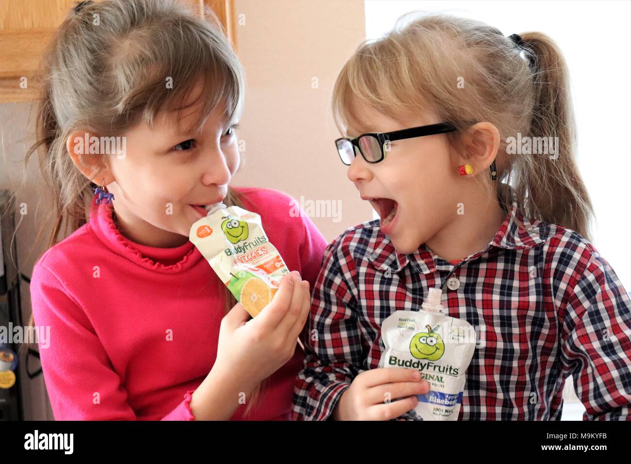 Sisters enjoying Buddy Fruits in the kitchen Stock Photo