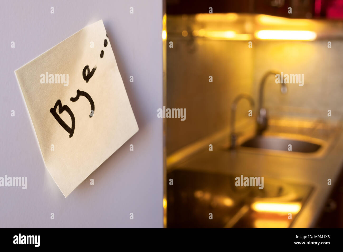 End of relationship concept: a goodbye note on a refrigerator with kitchen appliances and yellow lights in blurred background Stock Photo