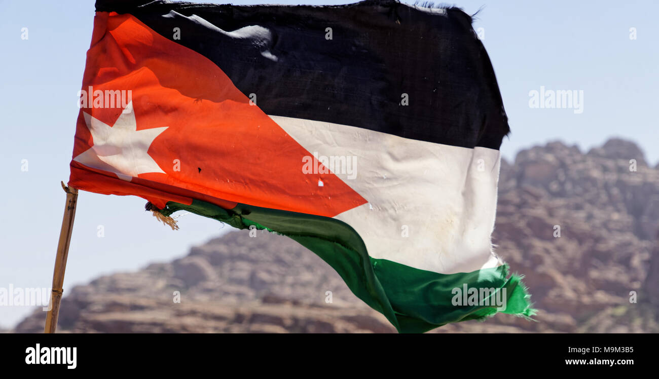Slightly battered flag of the land Jordan on the high windy cliffs of Petra, Wadi Musa, Jordan, middle east Stock Photo