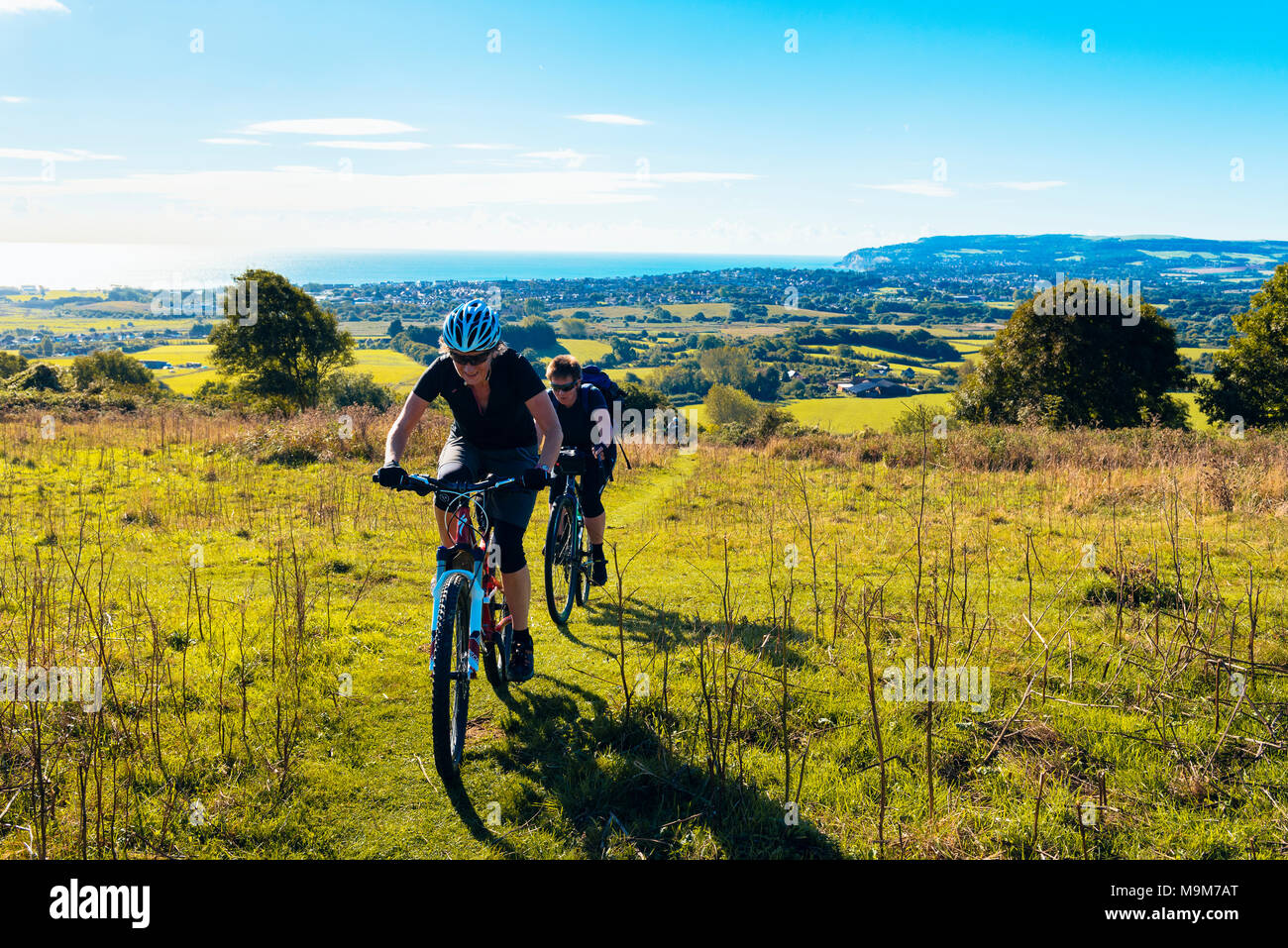 Two female cyclists climb onto Brading Down between Sandown and Ryde in the Isle of Wight, one on a mountain bike, one on a gravel bike Stock Photo