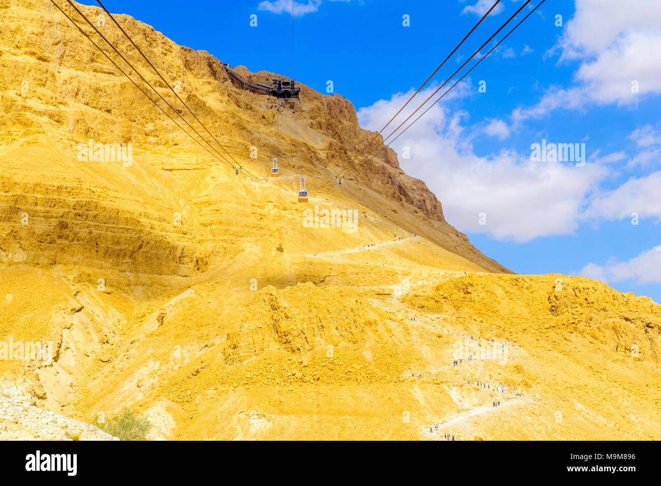 MASADA, ISRAEL - MARCH 16, 2018: The cliff and fortress of Masada, cable cars and visitors climbing the snake path, on the eastern edge of the Judaean Stock Photo