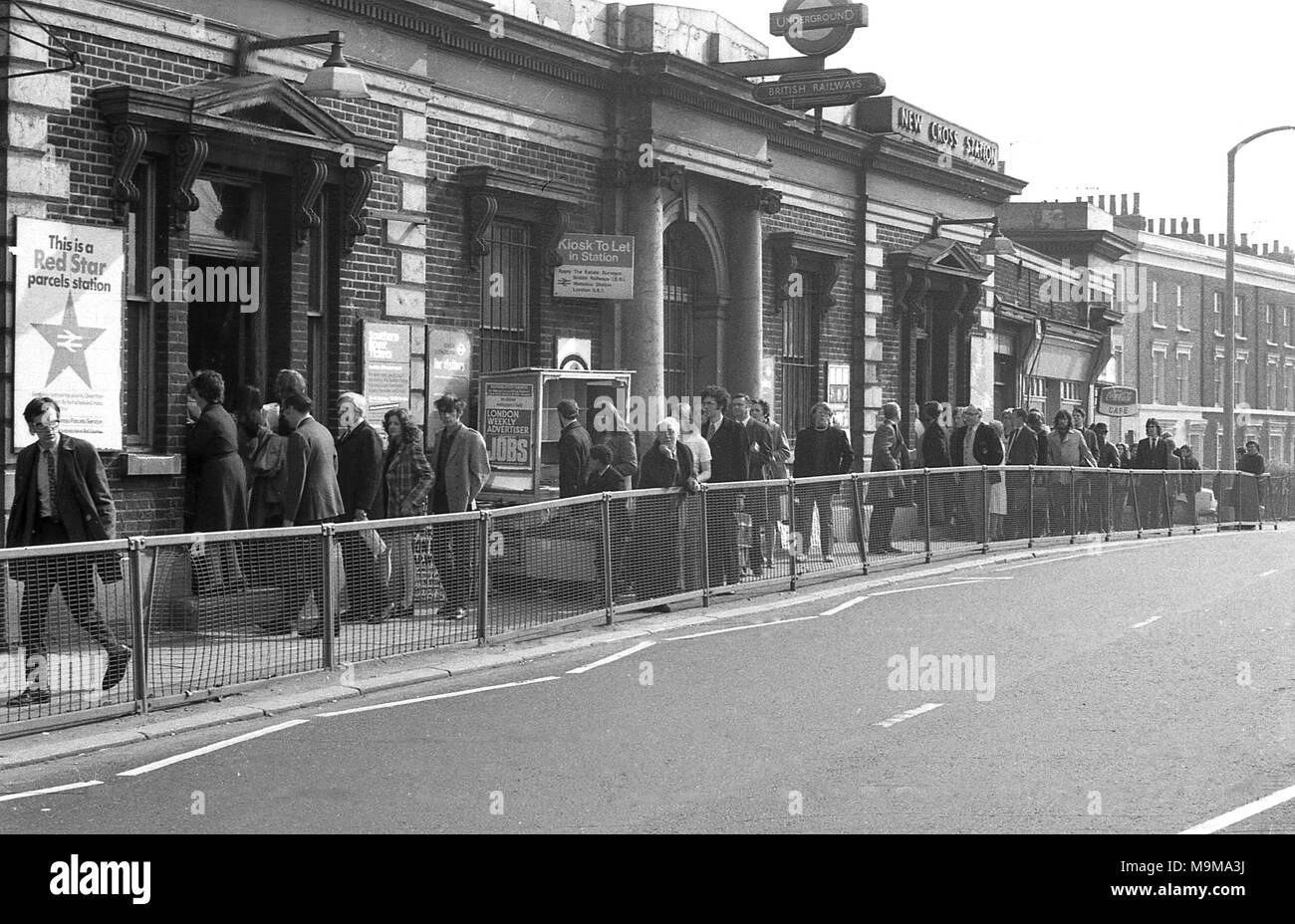 1973, New Cross Railway Station, South East London, a long line of commuters queuing up on the pavement outside waiting to enter the railway station due to overcrowding on the platforms because of cancelled trains. Stock Photo