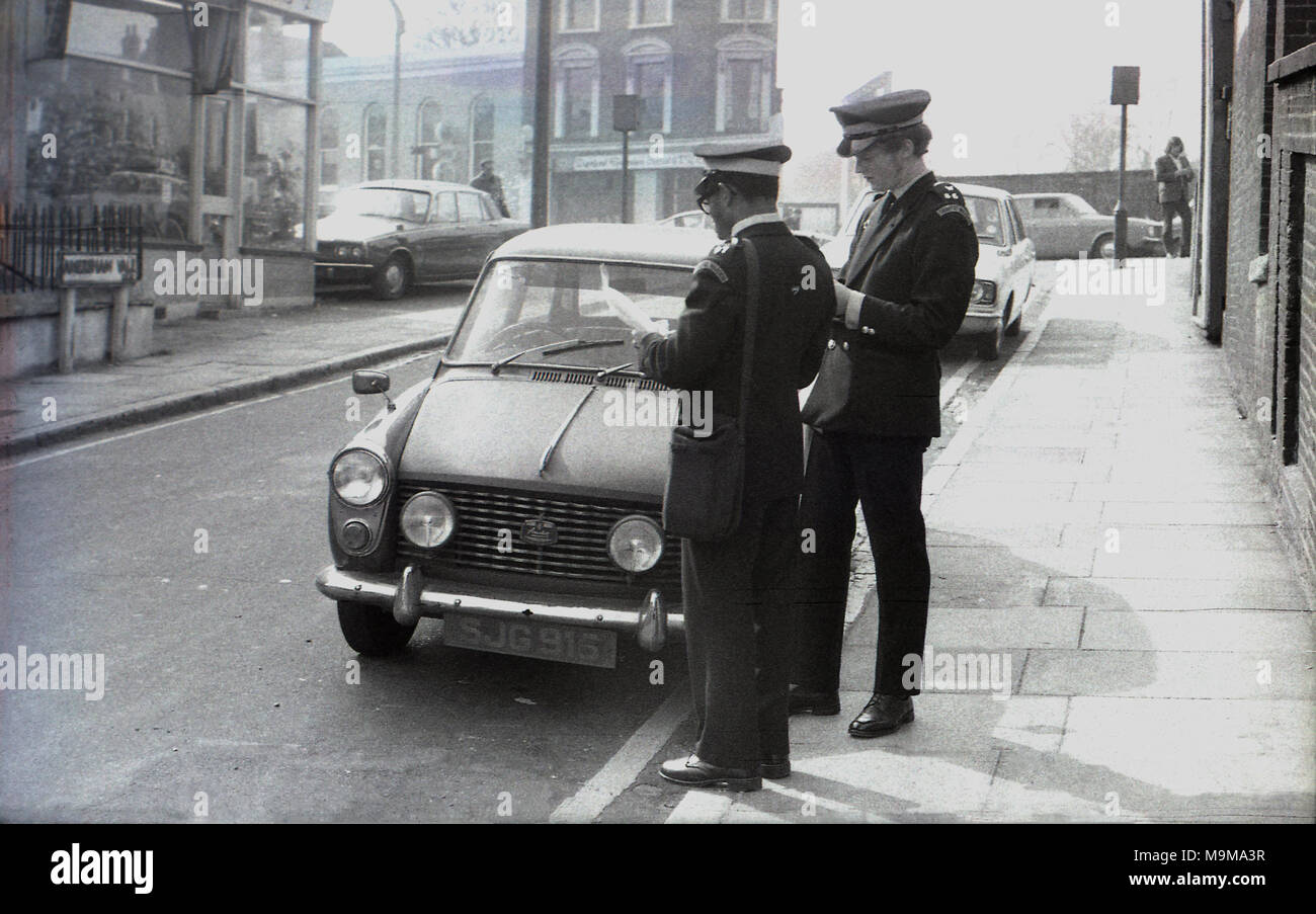 1970s, historical, two male traffic wardens standing on the pavement by a small motorcar parked in a side street near New Cross Railway station in South East London, England. Stock Photo