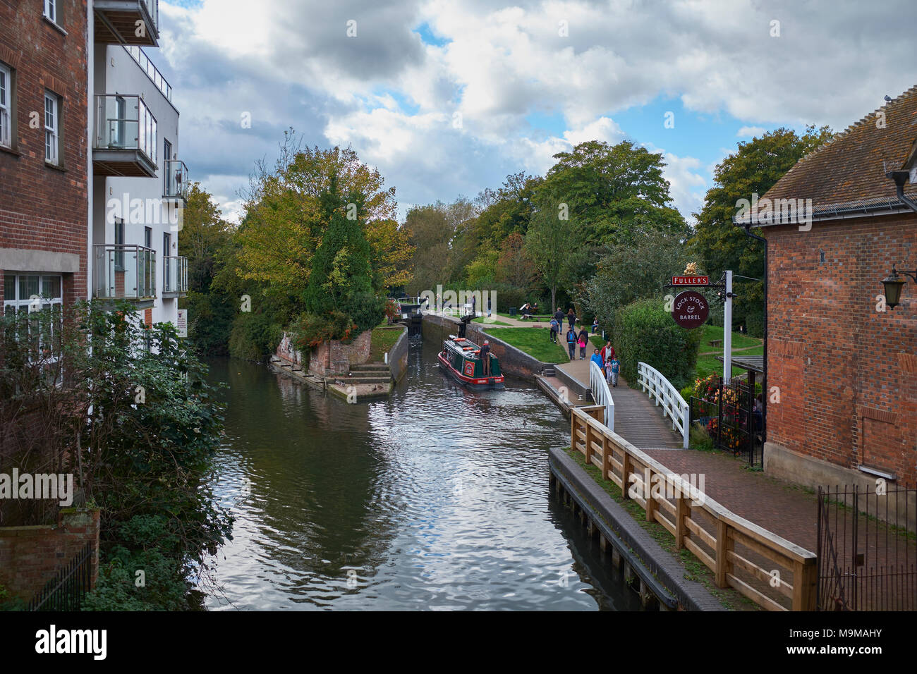A barge traveling along the Kennet and Avon canal through the town of  Newbury, West Berkshire, with buildings both sides and people walking on a path Stock Photo