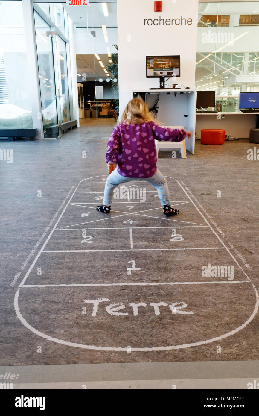 A little girl (3 yrs old) playing hopscotch on an indoor hopscotch game in a public library in Quebec Canada Stock Photo