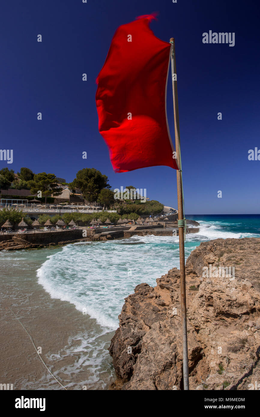 Red bathing warning flag blowing in the wind at Cala Molins beach, Mallorca, Spain Stock Photo