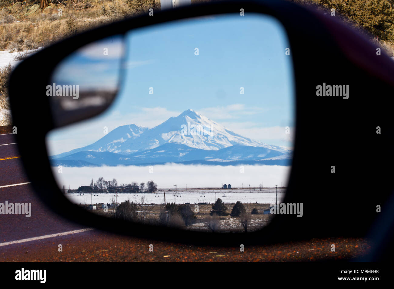 The snowy summit of Mount Shasta stands tall in a car door sideview mirror in Northern California in Winter Stock Photo