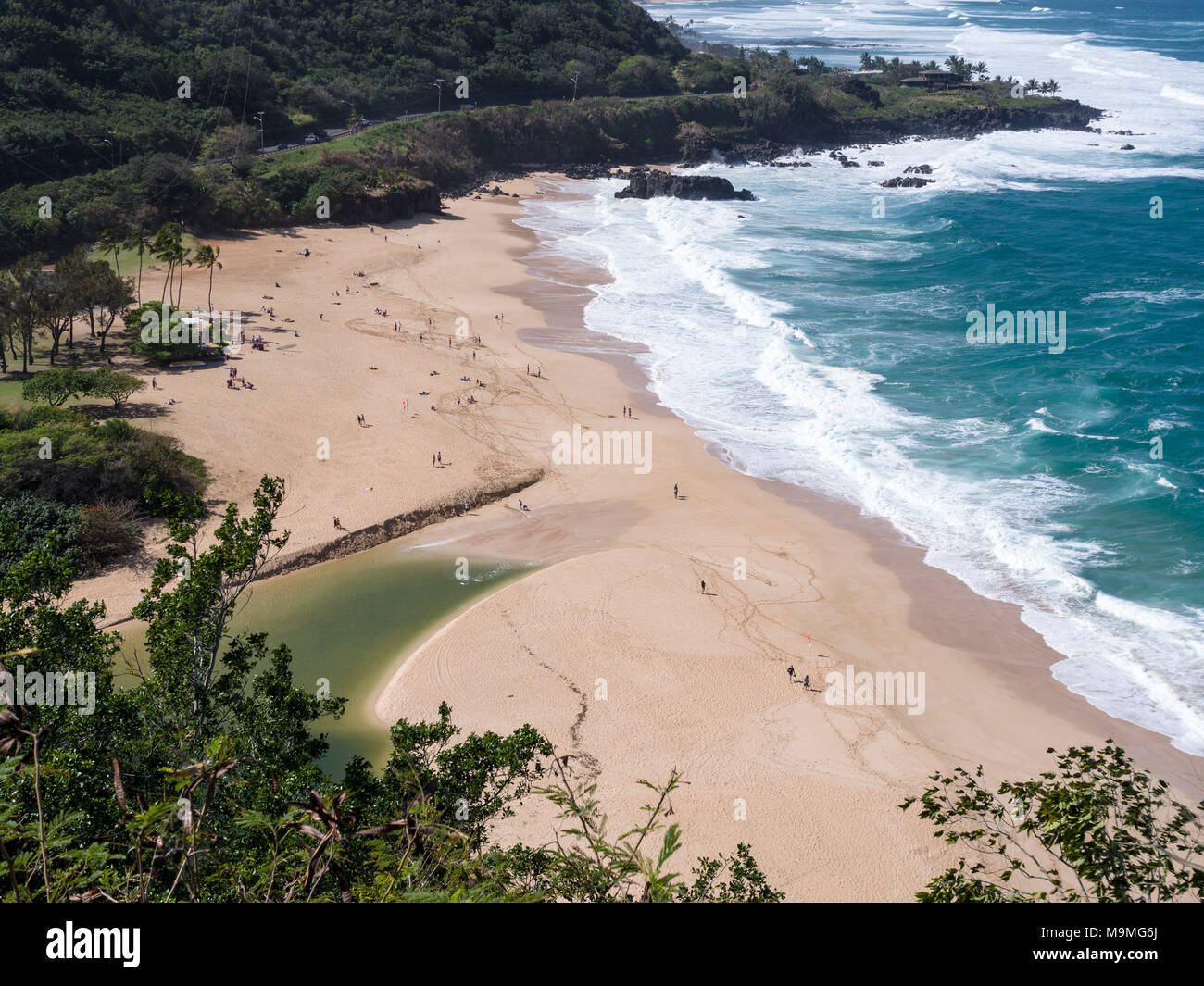 Waimea Bay Beach Park from high above: The fine sand of Waimea Bay beach populated by many beach goers watching the wavews. None swimming due to the heavy swell in the blue ocean waters. Stock Photo