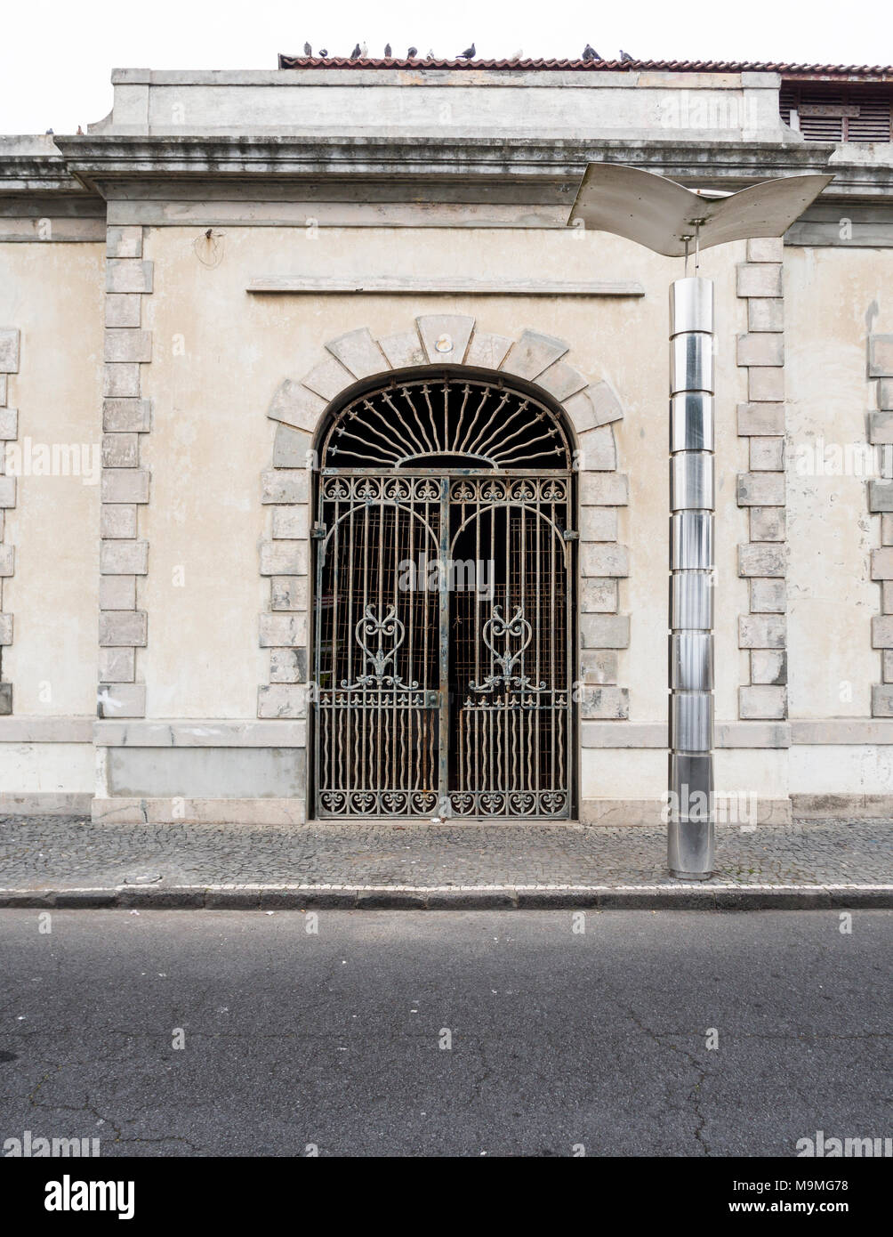 Abandoned Gate, Modern Street Lamp: The rusting gate of an abandoned building contrasts with the modern shiny new street light on the street outside. Stock Photo