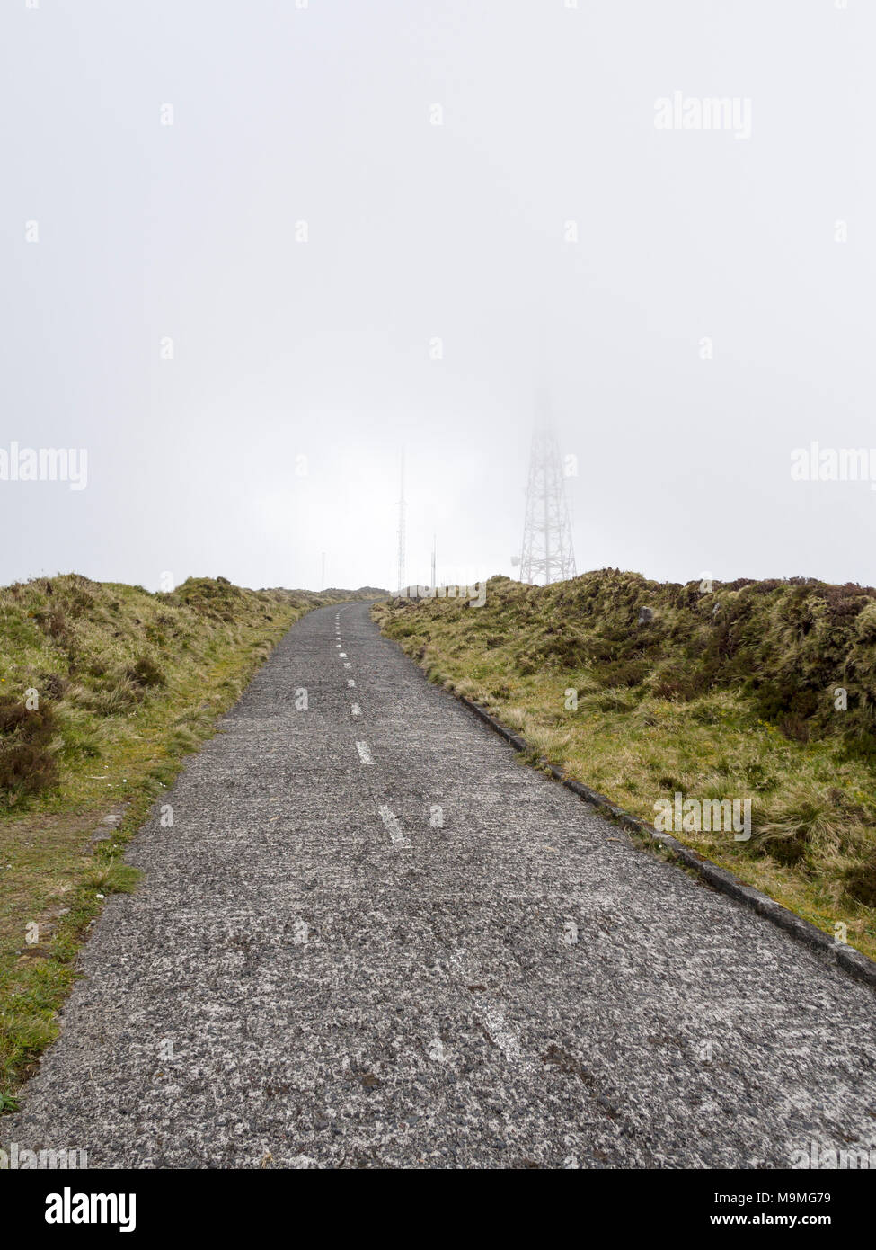 High Road to the Clouds: A small paved road curves toward some fog enshrouded communication towers high on the hills above Lagoa do Fogo. Stock Photo