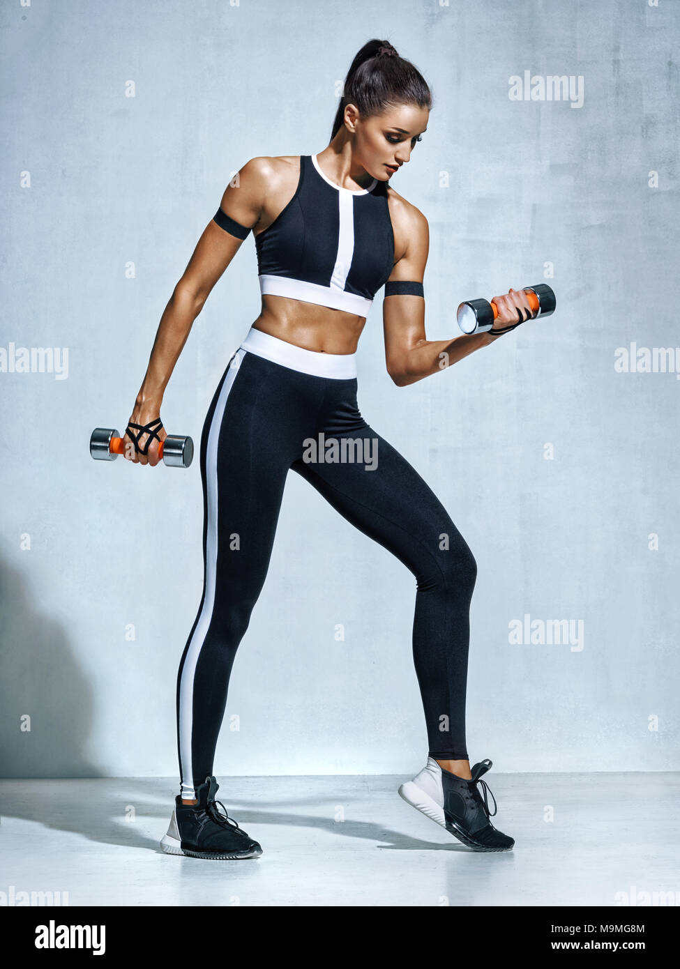 Athletic woman doing exercise for arms. Photo of muscular fitness model  working out with dumbbells on grey background. Strength and motivation  Stock Photo - Alamy