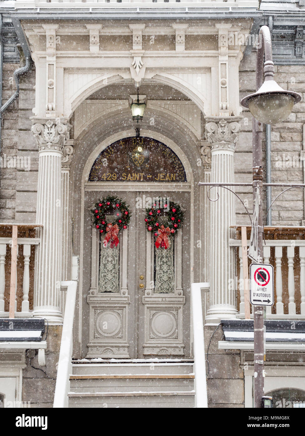 A pair of decorated doors in the snow: The entrance to 429 Saint Jean decorated by two matching wreaths over the double doors. Fancy columns and a porch protect them from the falling snow. Stock Photo