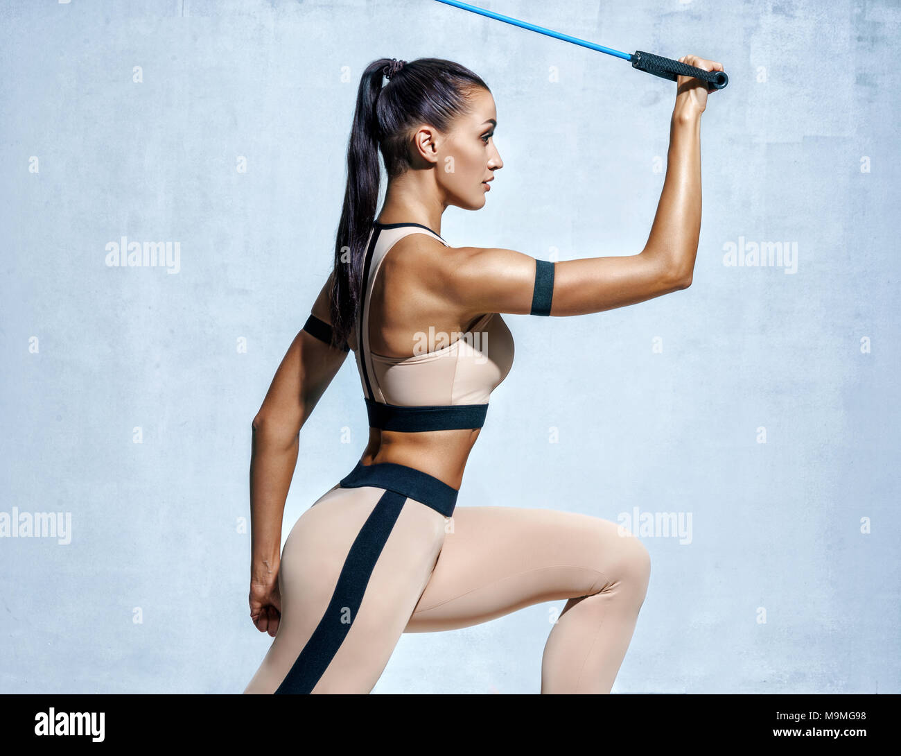 Strong woman using resistance band in her exercise routine. Photo of fitness model workout on grey background. Strength and motivation Stock Photo