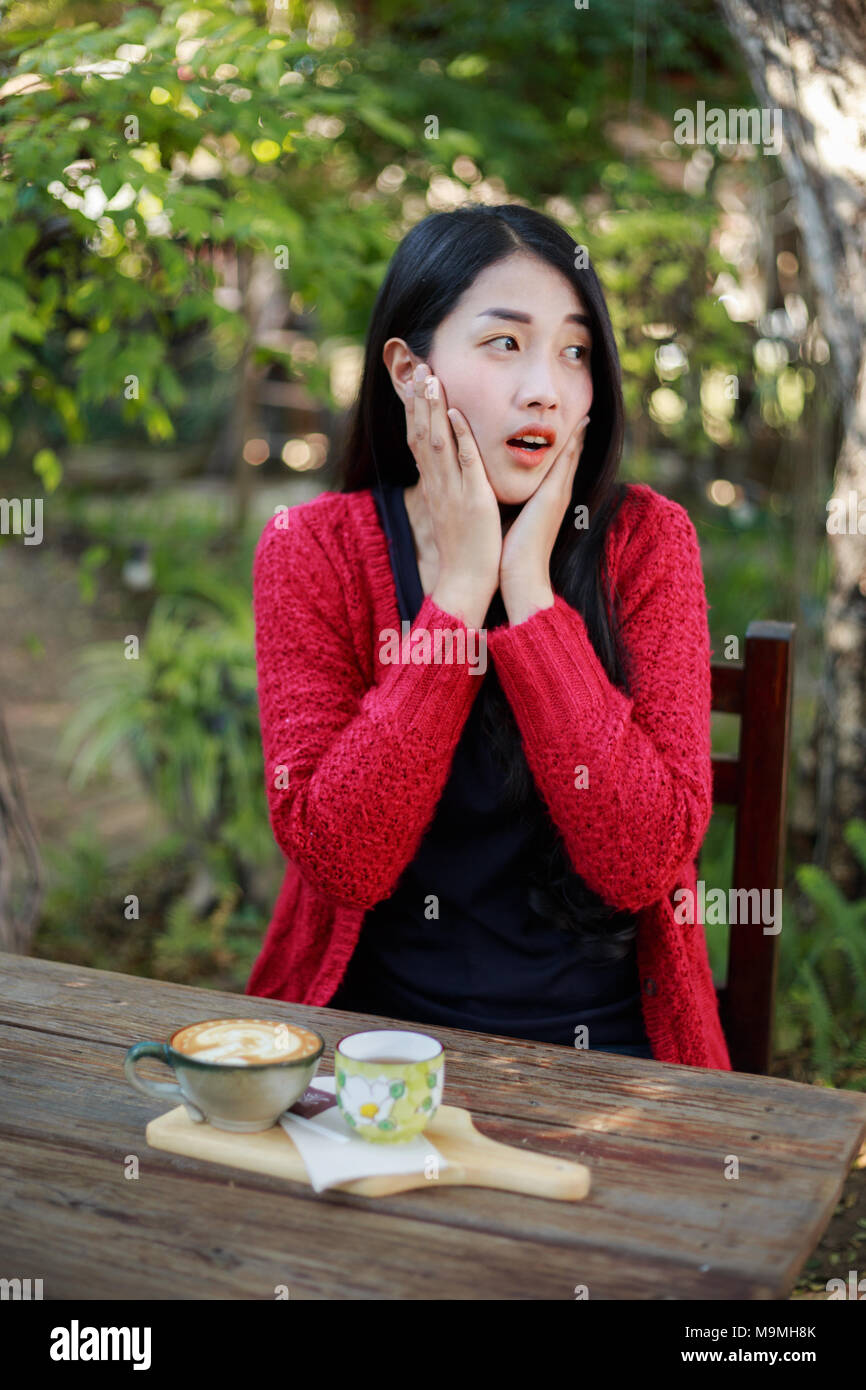 Portrait of a shocked young woman sitting on table with coffee in the garden Stock Photo