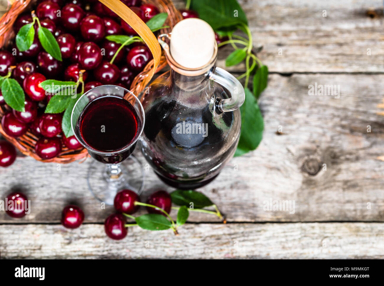 Glass of alcohol tincture made from cherry fruits, liquor in a bottle on rustic background Stock Photo