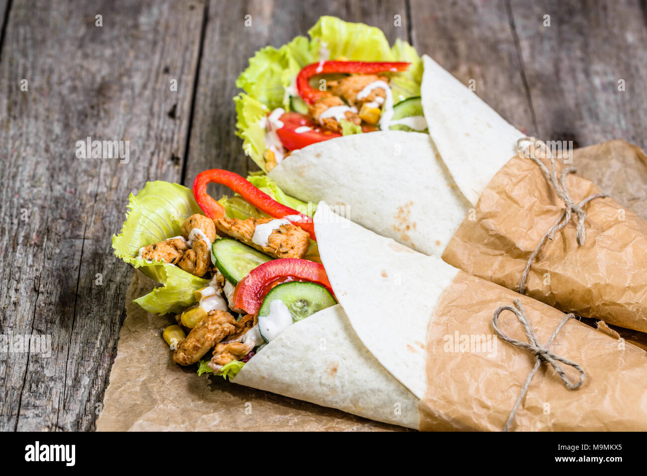 Mexican fajitas, tortilla wraps filled with fresh vegetables and grilled chicken on rustic wooden table Stock Photo
