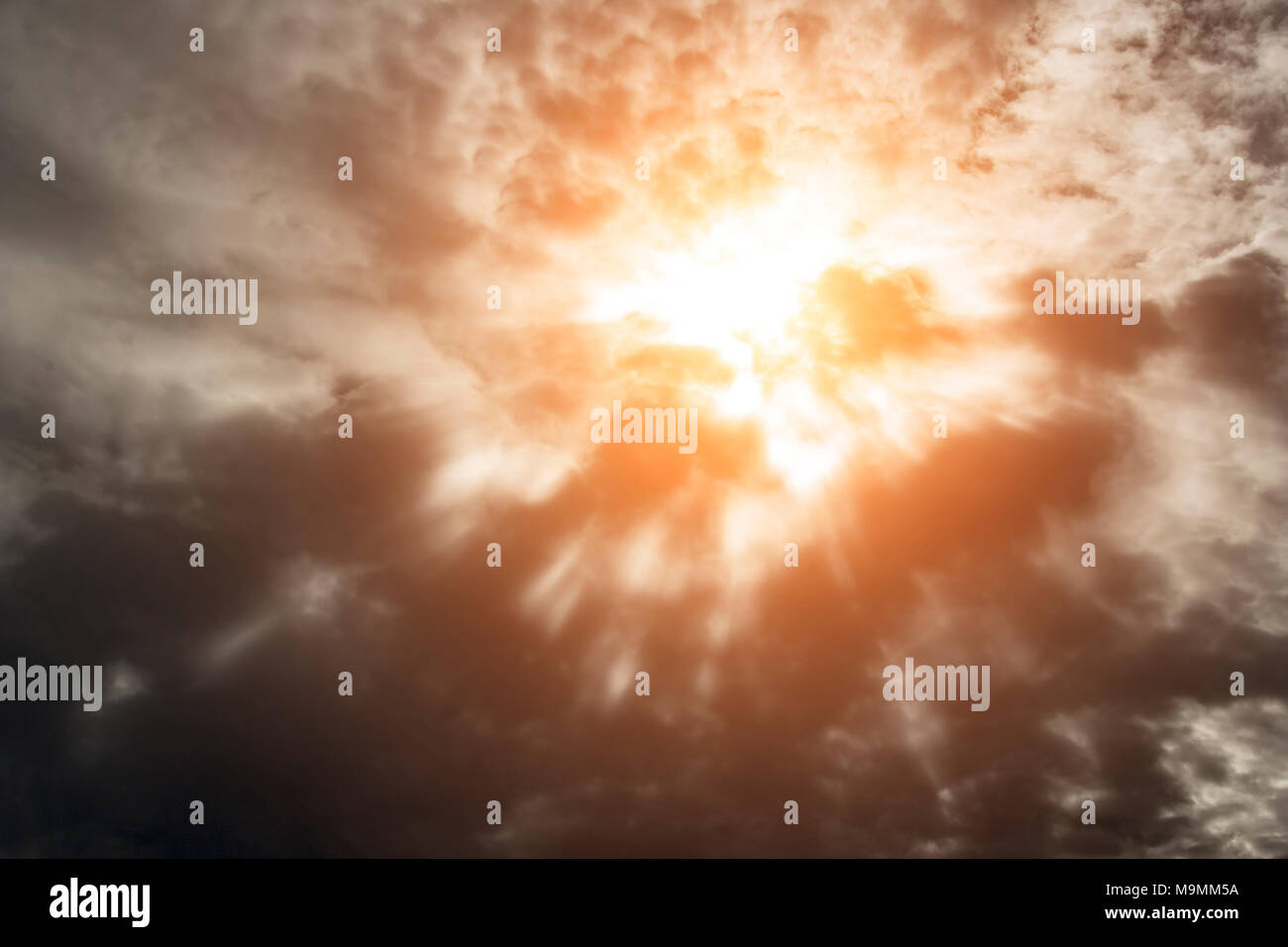 Dramatic background with warm sun rays penetrating dark clouds. Stock Photo