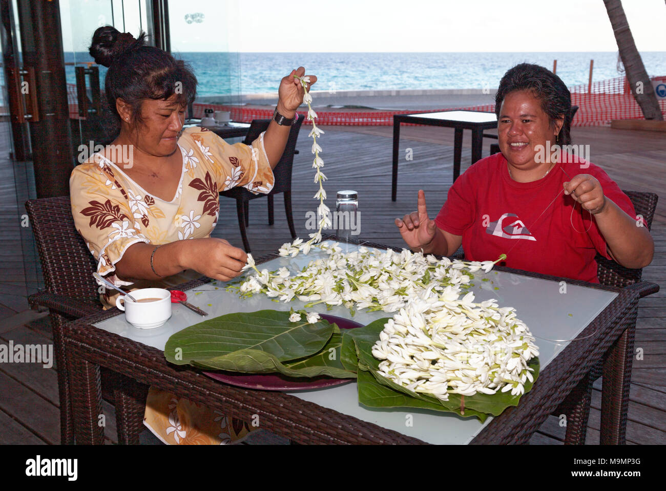 Two women, Polynesian, threads white blossoms, flowers to necklaces, Rangiroa, society islands, Windward Islands Stock Photo