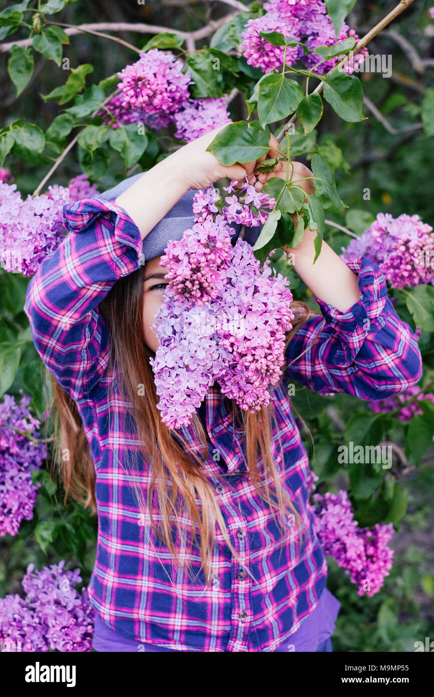 Photo of young model girl in colorful shirt hiding her face in summer lilac garden Stock Photo