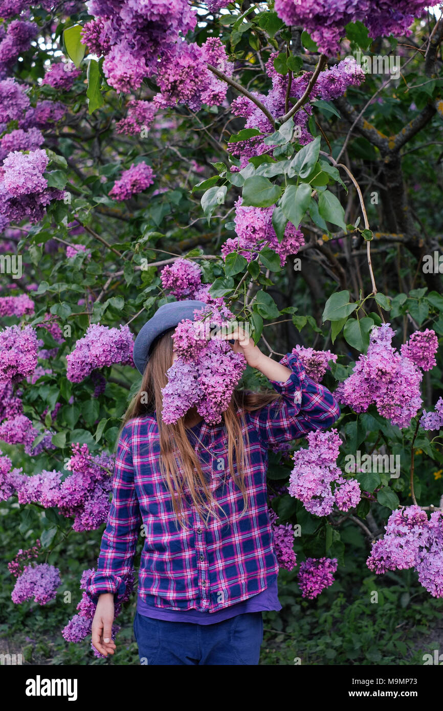 Photo of young model girl in colorful shirt hiding her face in summer lilac garden Stock Photo