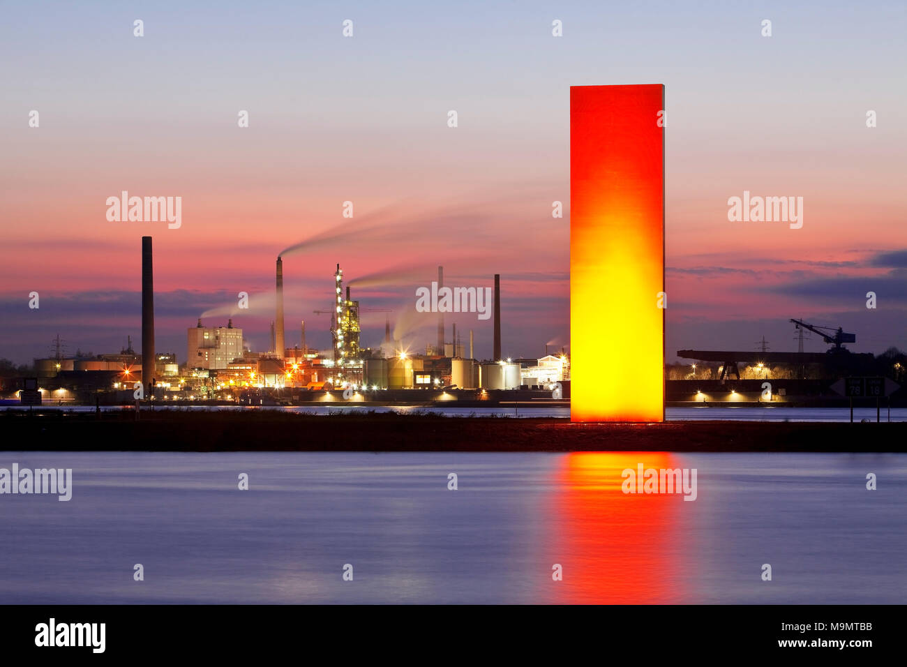 Illuminated sculpture Rheinorange in the sunset in front of industrial panorama, Rhine, Duisburg, Ruhr Area Stock Photo