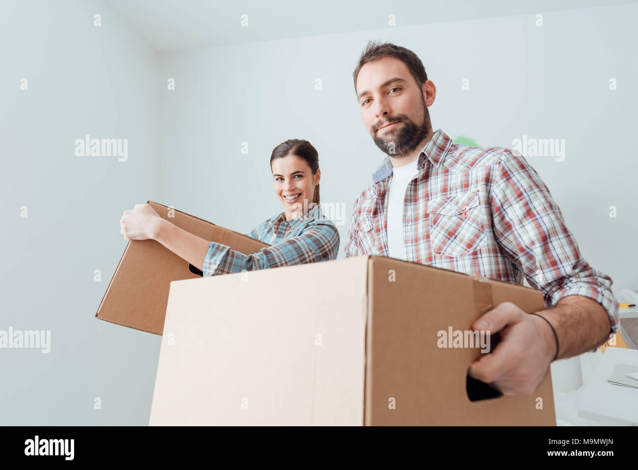 Young smiling couple moving into a new house, they are carrying full ...
