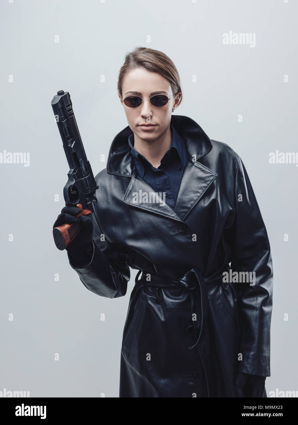 Cool female spy agent in black leather coat, she is holding a gun and posing Stock Photo