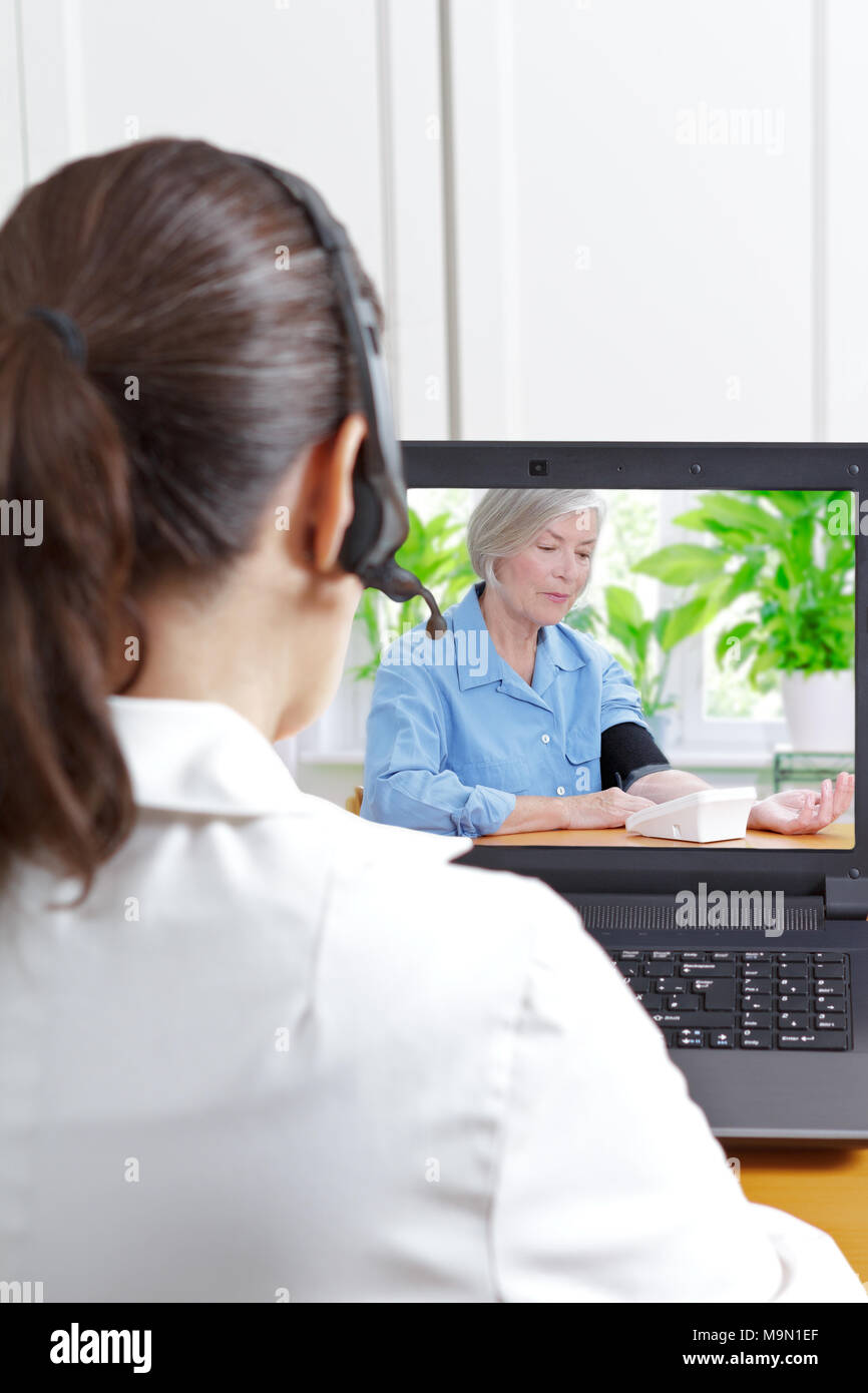 Female doctor with headset in front of her laptop during a video call with an elderly patient measuring her blood pressure Stock Photo