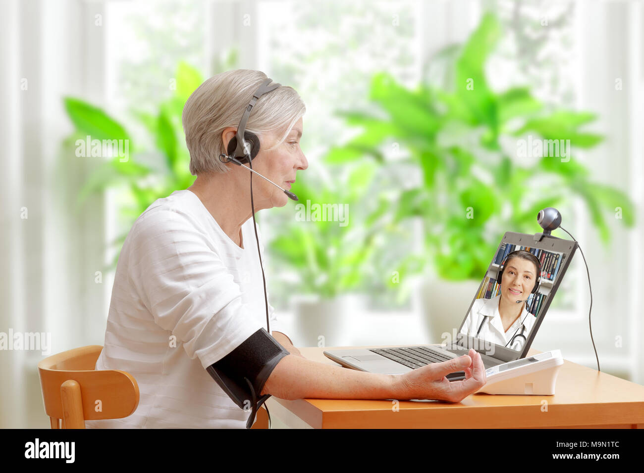 Senior woman in her living room in front of a laptop checking her blood pressure during a video call with her doctor of cardiology Stock Photo