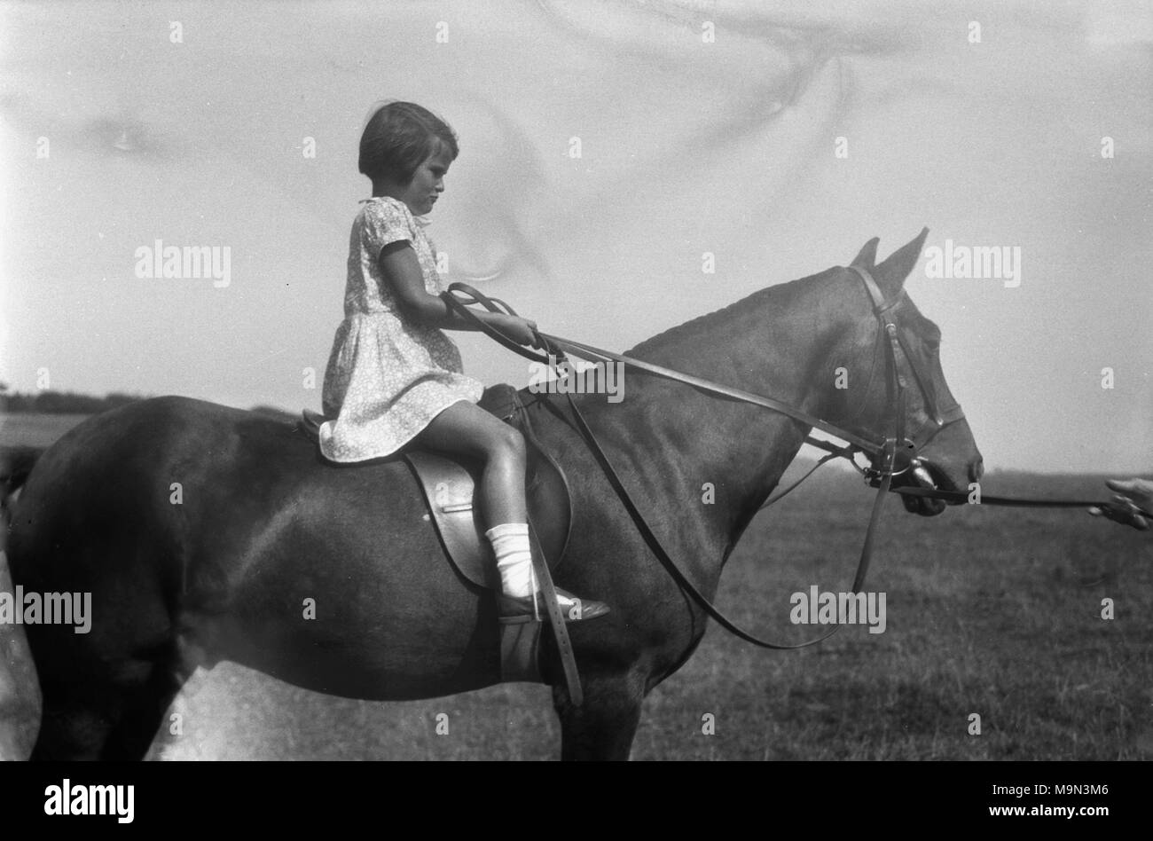 1920s, historical picture, rural life in England, before the arrival on mass of the motorcar, meant that most youngsters living in the country side learnt to ride horses from an early age and here we see a young girl doing exactly that. Wearing a dress, she is sitting on and holding the reins of a large horse. Stock Photo