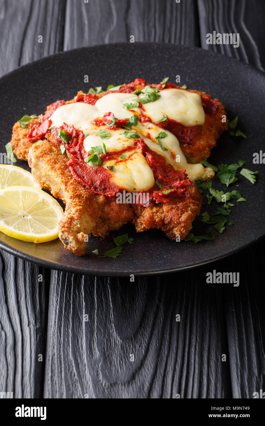 Milanesa a la napolitana - veal cutlet with mozzarella cheese and tomato sauce close-up on a plate on a table. Vertical Stock Photo