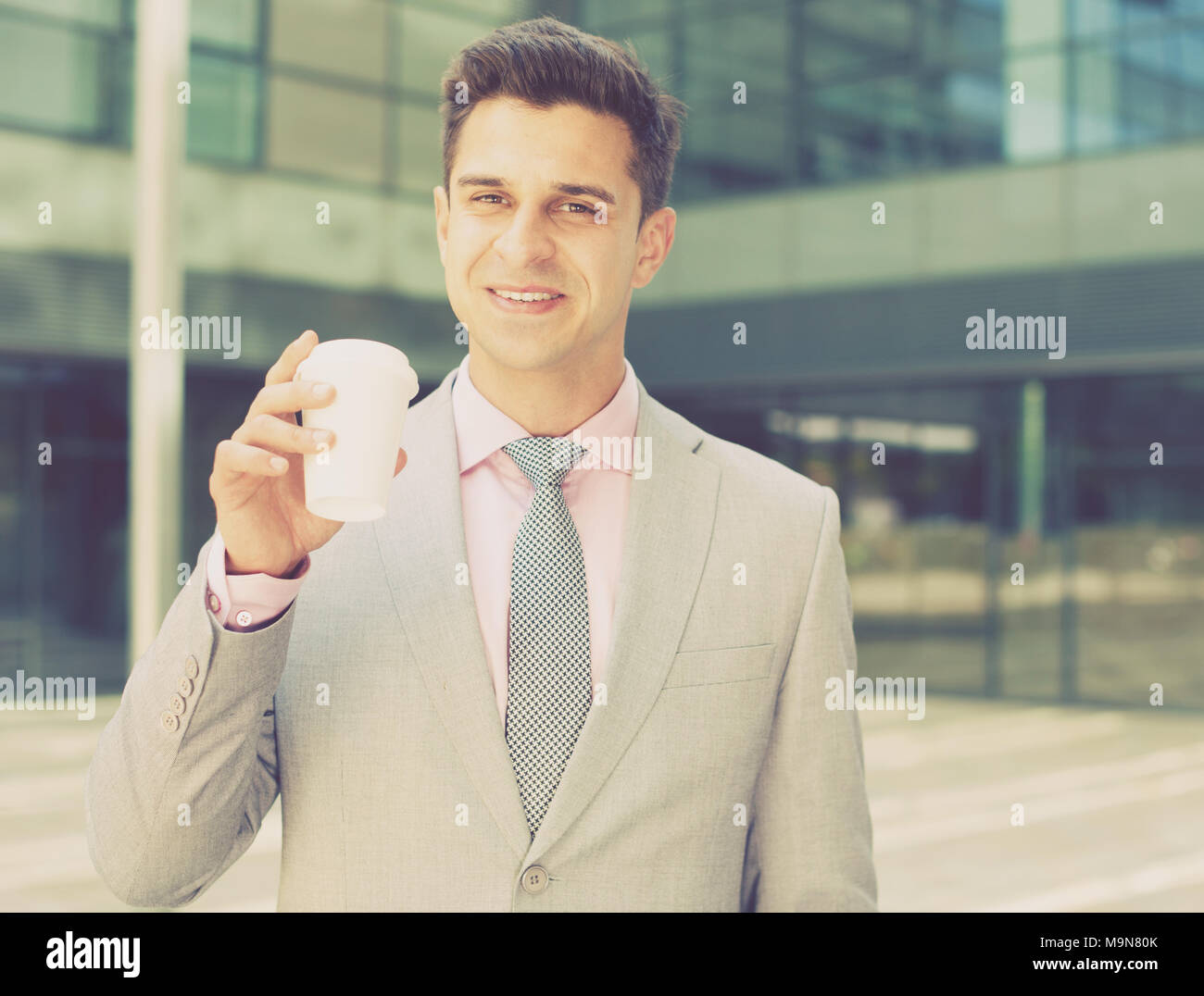 Portrait of young successful businessman drinking coffee near large ...