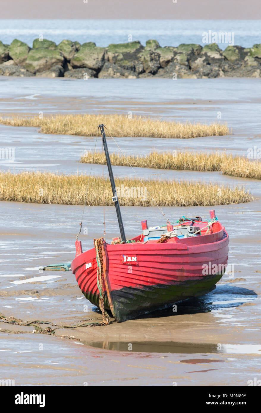 A small red inshore fishing boat aground and waiting for the tide at Morecambe, England, UK Stock Photo