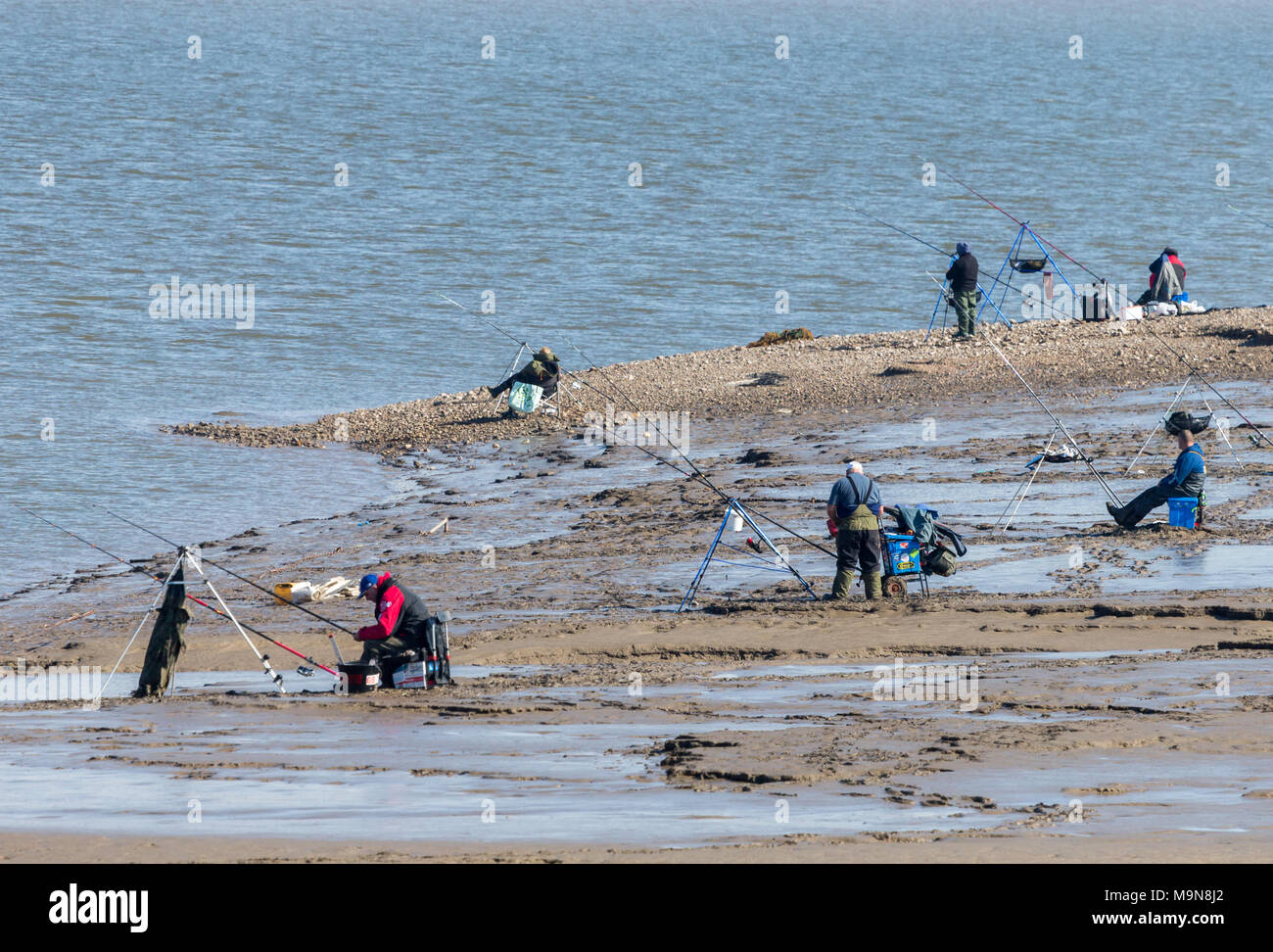 A group of sea-anglers fishing off the beach at Morecambe. The tide is out and they are sat on the shoreline. Stock Photo