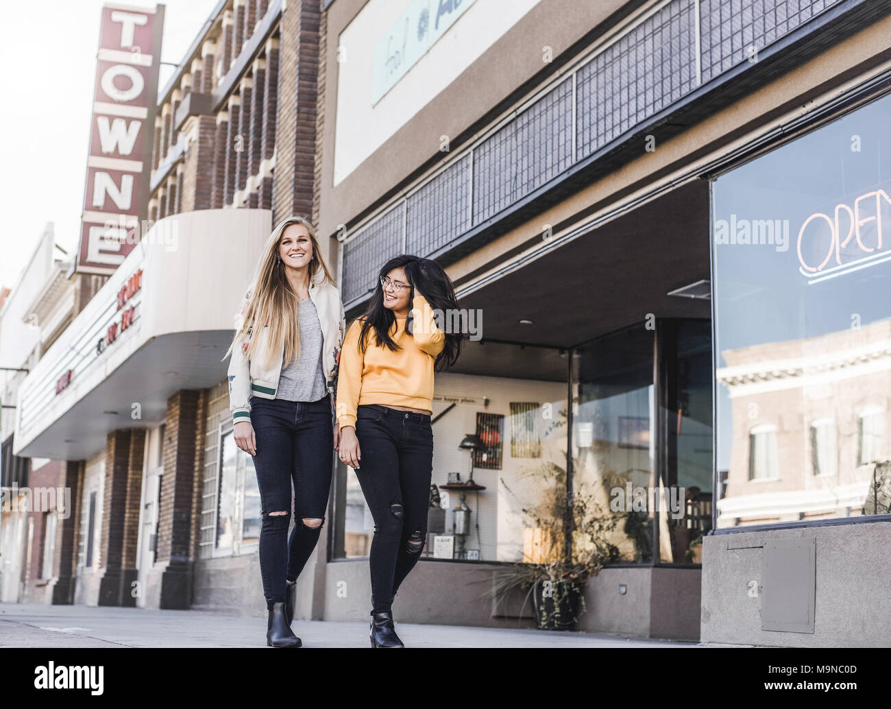 two pretty teenage girls laughing and walking down a street downtown Stock Photo