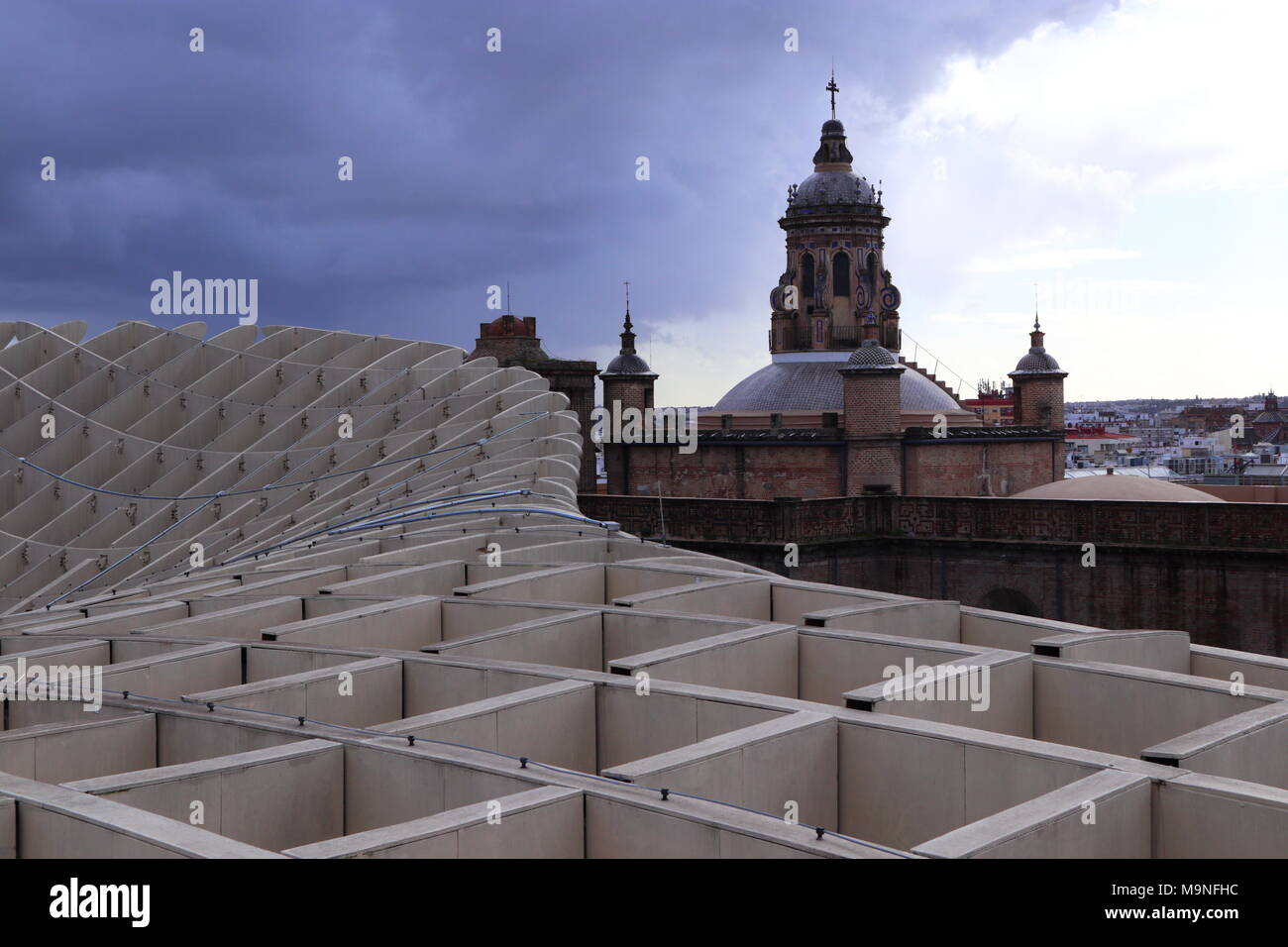 View from Metropol Parasol, modern architecture with an old church in the foreground, curved shape, dramatic sky, dark cloud, Seville, Spain Stock Photo